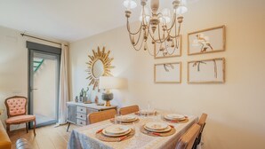 Comedor con mesa preparada para cuatro, una araña, obra de arte en la pared y un espejo con forma de sol.