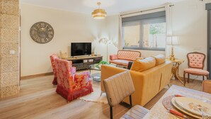 Una sala de estar con sofá, sillones, televisor, un reloj decorativo y una ventana.