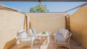 Un patio techado con mobiliario de mimbre y una mesa, con una pared de piedra y un cielo despejado.