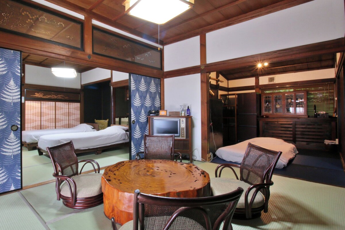 A traditional Japanese-style room with tatami flooring, a round wooden table, and two tatami mats with cushions.