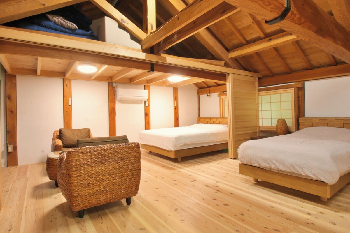 A wooden interior with a bed, a wicker chair, and a sofa.