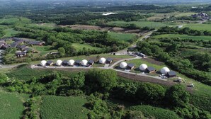 An aerial view of a rural area with several dome-shaped buildings, surrounded by lush greenery and fields. - Resonate Glamping Hoshi no Oka (Taketa)