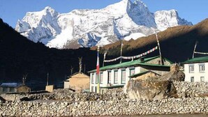 Paesaggio montuoso con una cima innevata sullo sfondo, un edificio con tetto verde e un muro di pietra in primo piano.