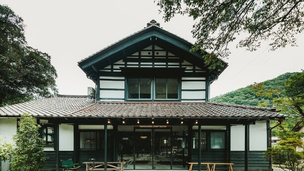 Un edificio japonés tradicional con techo de tejas, entrada cubierta y un pequeño jardín con bancos.