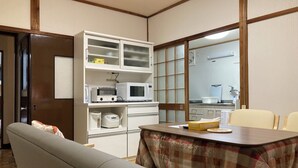 A compact kitchen with a microwave, toaster, and rice cooker on white cabinets, a dining table with a plaid tablecloth, and a bench. - Granny's House (Kozagawa)