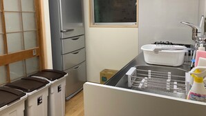 A compact kitchen with a refrigerator, a sink with a drying rack, and trash bins. - Granny's House (Kozagawa)