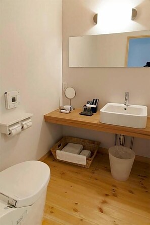 Ein Badezimmer mit Toilette, Waschbecken, Spiegel und einer kleinen Holzablage mit Toilettenartikeln.