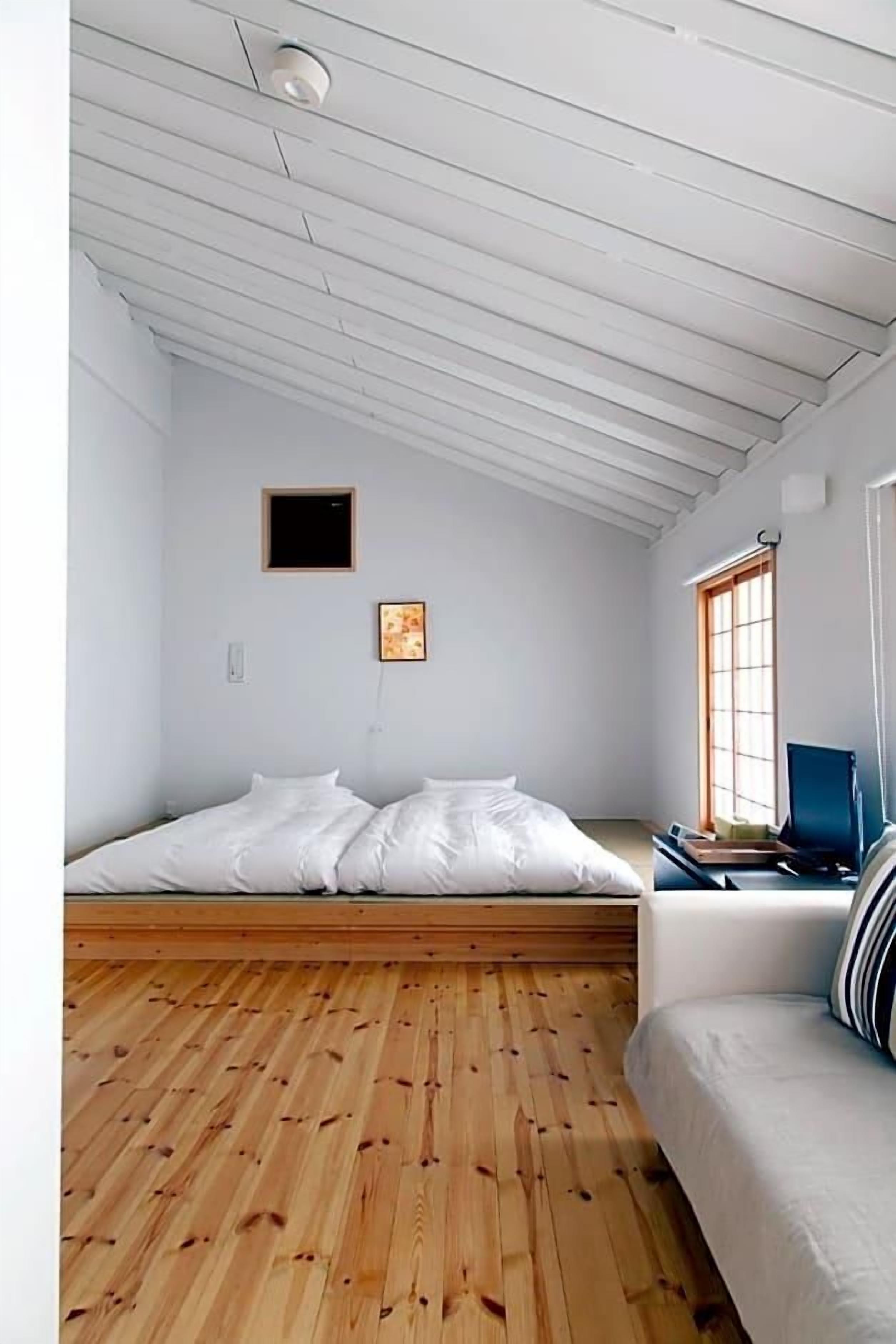 Una habitación con techo inclinado, una cama, piso de madera, un ventanal y una silla.