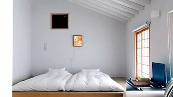 Una habitación con techo inclinado, una cama, piso de madera, un ventanal y una silla.