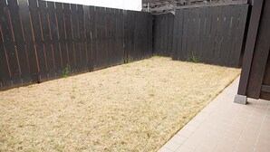 Een achtertuin met een zwart hek, een betegeld terras en een pergola.