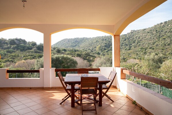 Una veranda coperta con tavolo e sedie, affacciata su un paesaggio montano.