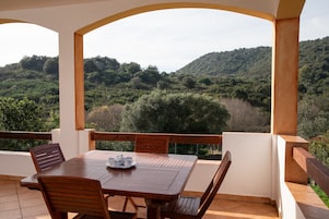 Un área de comedor al aire libre techada, con una mesa y sillas, con vistas a un paisaje montañoso.
