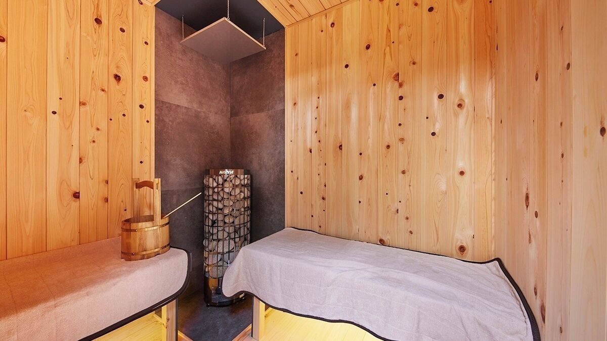 A sauna room with wooden walls and benches, a stone wall, and a wooden bucket.