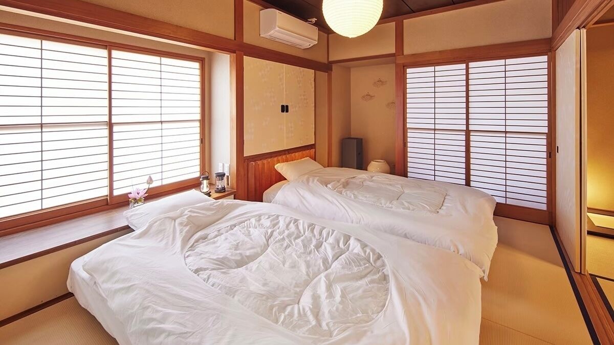A traditional Japanese-style room with tatami flooring, a low wooden bed, sliding shoji doors, and a ceiling fan.