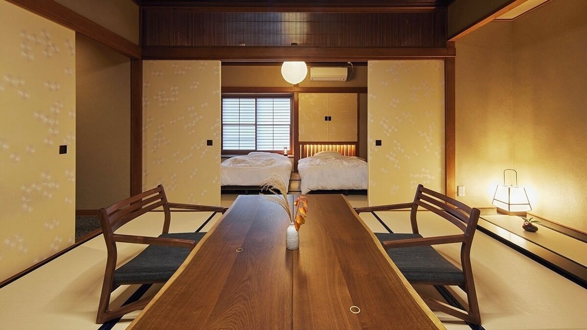 Habitació japonesa tradicional amb taula de fusta, dos llits i una làmpada.