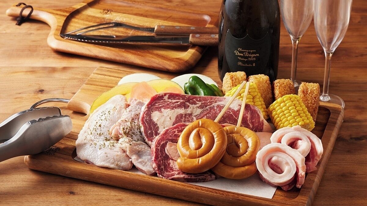 Une planche à découper en bois, sur laquelle on voit différentes sortes de viandes, des légumes et une bouteille de champagne.
