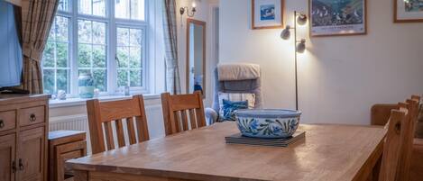A dining area with a wooden table, chairs, a bowl, and a chair with a cushion.