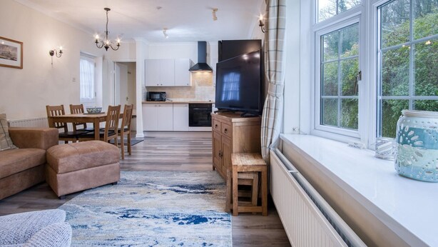 A cozy living room with a sofa, a TV, and a dining area with chairs and a table. - Garden Cottage - 2 Bedroom Cottage - Penally (Tenby)