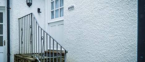 A white building with a stone staircase leading to a door, a black metal railing, and a small sign on the wall.