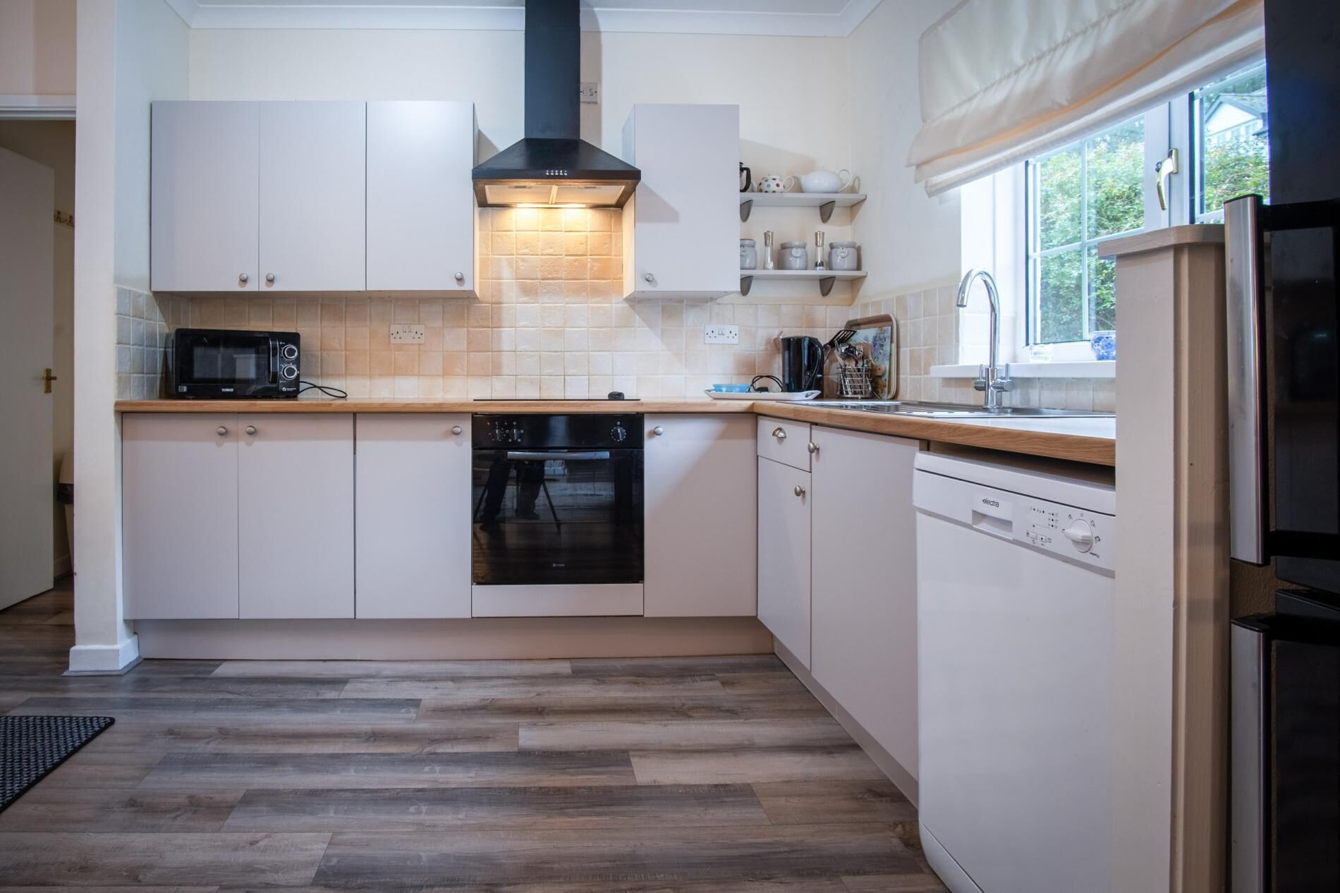 A modern kitchen with white cabinets, a black oven, a dishwasher, and a window with a view of greenery.