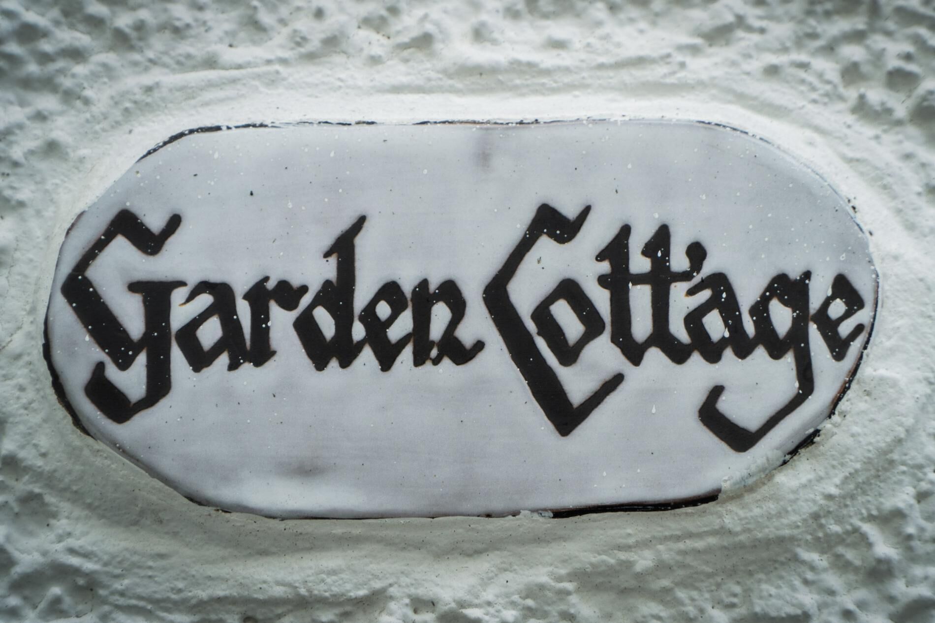 Un panneau blanc, de forme ovale, sur lequel on peut lire les mots « Garden Cottage » écrits dans une police de caractères stylisée.