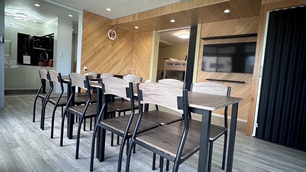 A modern dining area with a long table and chairs, wooden panel walls, and recessed ceiling lights.