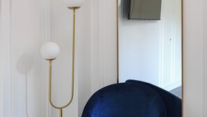 Una habitación con una butaca de terciopelo azul, una lámpara de pie dorada y un espejo grande en la pared.