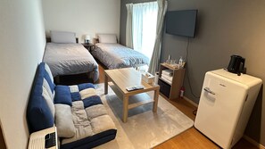 Habitación de hotel compacta con cama, sofá, una mesita, televisor y refrigerador.