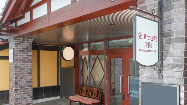 A hotel entrance with a bench outside, a signboard, and a brick wall. - Lodge Yaedake Sanso (Aizuwakamatsu)