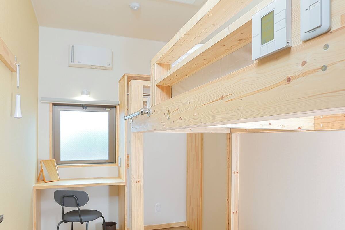 Une petite pièce comprenant un lit superposé, un bureau avec une chaise, une fenêtre et un luminaire au plafond.