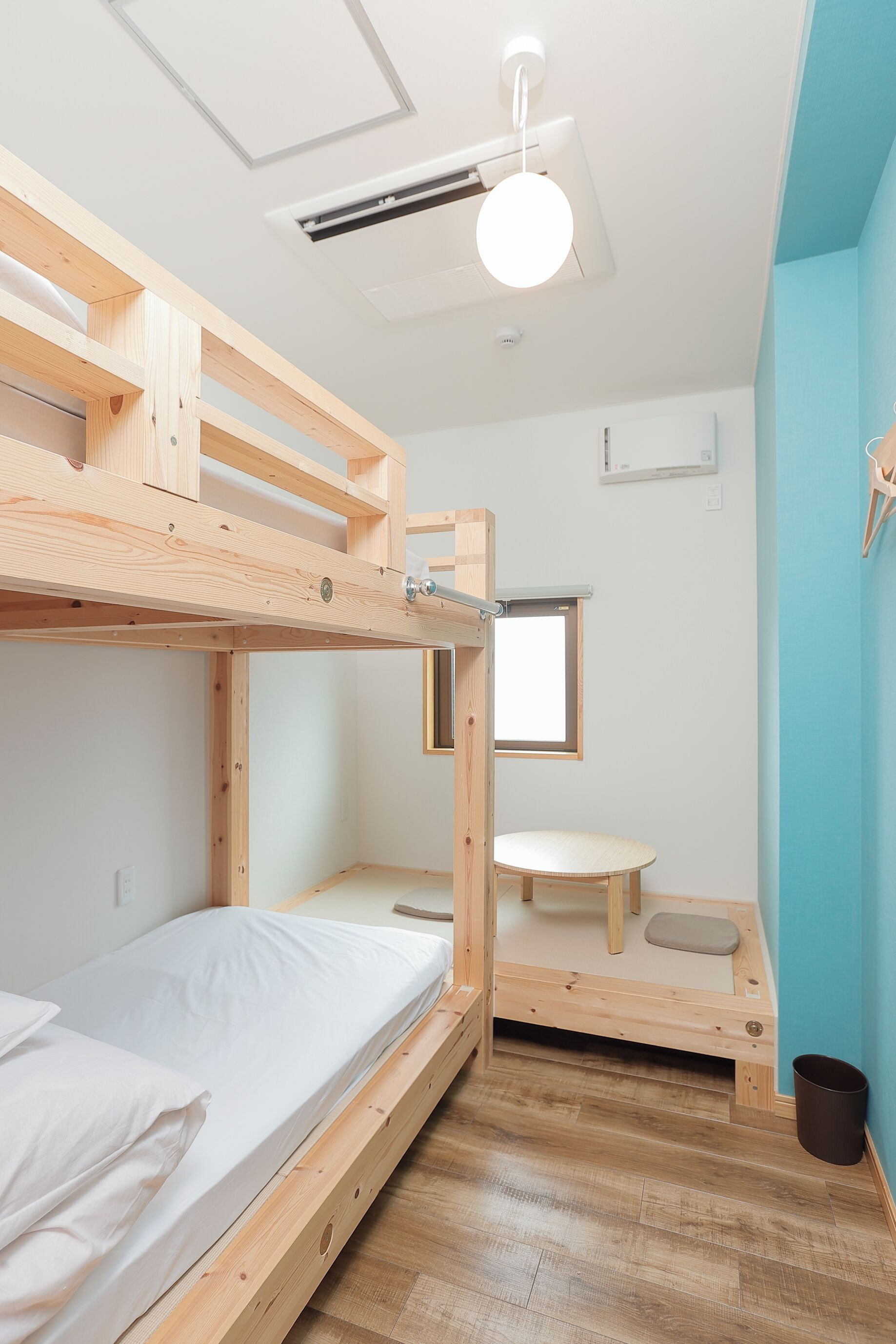 A bunk bed with a wooden frame, a small table, a window, and a ceiling light fixture.