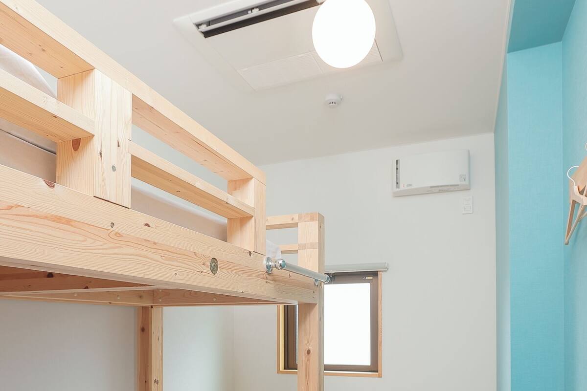 Un lit superposé avec une structure en bois, une petite table, une fenêtre et un luminaire fixé au plafond.