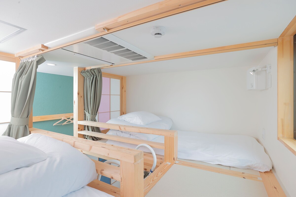 Une chambre avec un lit superposé en bois, une fenêtre avec des rideaux, un climatiseur fixé au mur et un petit miroir.