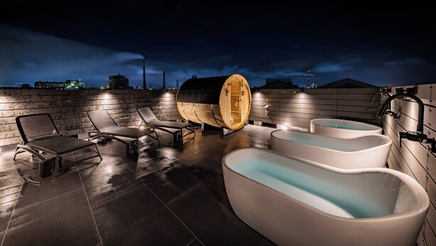 En avkopplande takterrass med solstolar, en trähusad bastu och flera bubbelpooler.