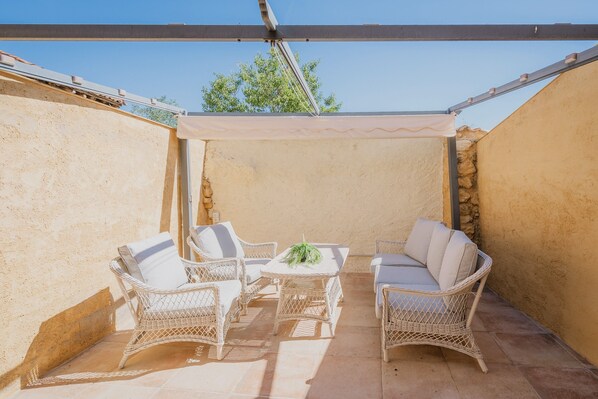 Ein überdachter Patio-Bereich mit Korbmöbeln und einem Tisch, mit einer Steinsäule und blauem Himmel.