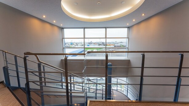 Un interior moderno con una escalera de cristal, un ventanal que ofrece vistas de la ciudad y una lámpara circular en el techo.