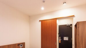 Habitación de hotel con cama, armario de madera, escritorio y puerta con cerradura y panel de control.