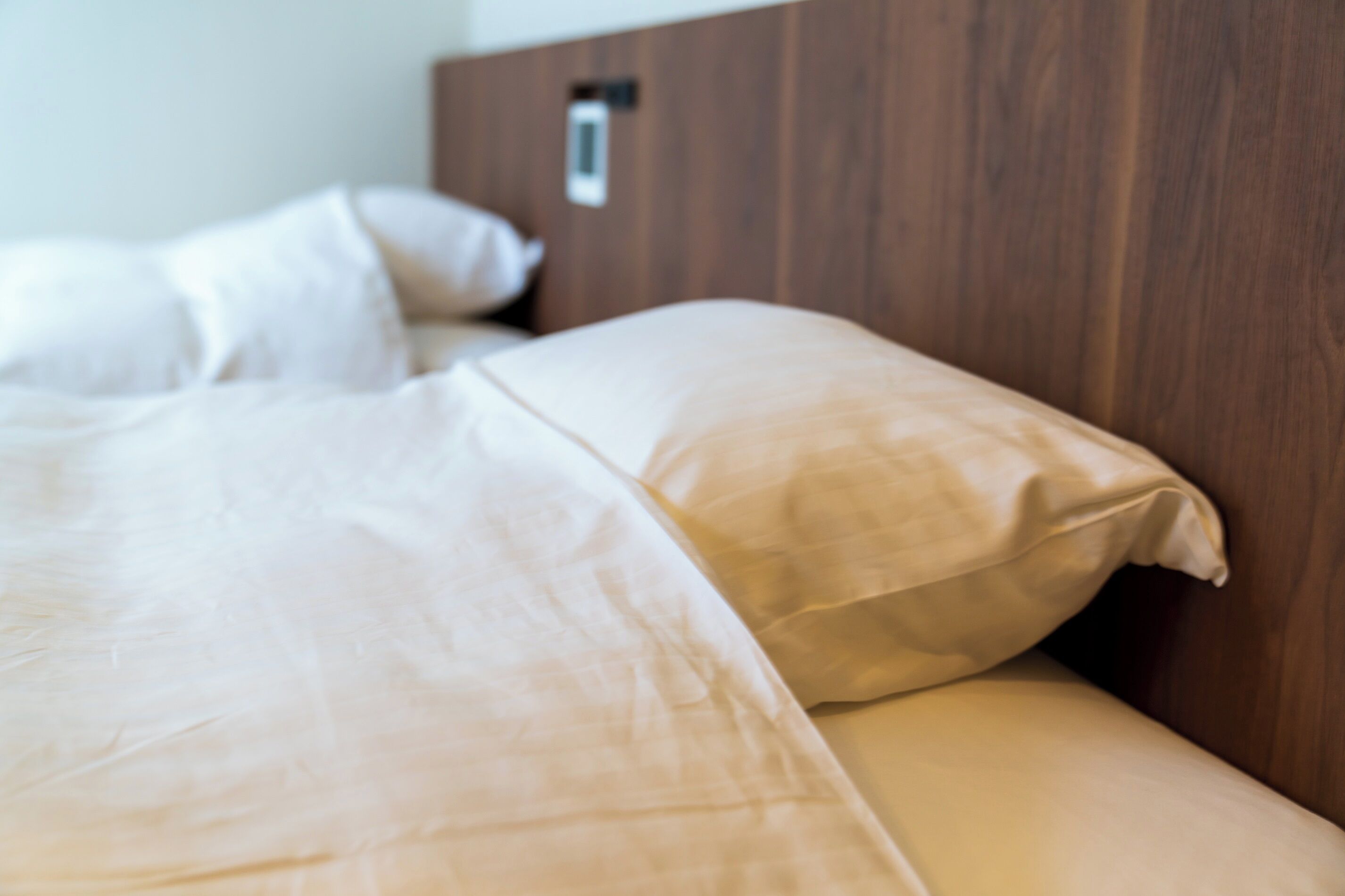 A neatly made bed with white bedding and a wooden headboard.