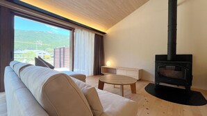 A modern living room with a sofa, a round table, and a wood-burning stove. - Centennial Forest Hotel Shiori (Nishiawakura)