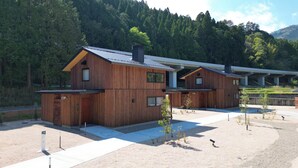 A modern wooden cabin with a sloped roof, a small porch, and a view of a forested mountain range. - Centennial Forest Hotel Shiori (Nishiawakura)