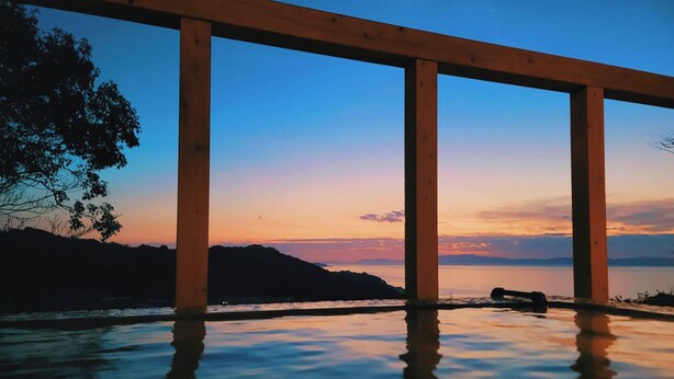 Un pontile in legno con vista su un tramonto riflesso in acque calme, con colline sullo sfondo.