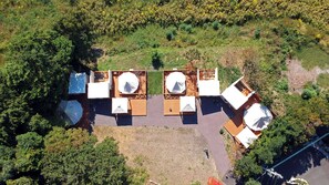 An aerial view of a campsite with multiple tents and a central wooden deck with tables and chairs. - Cocohare (Unzen)