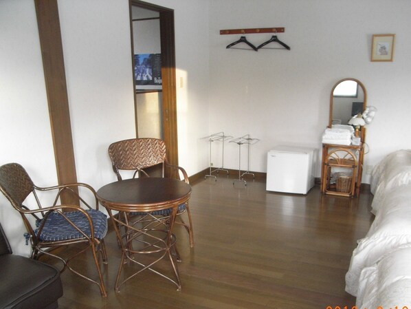 A room with a bed, a small white refrigerator, a wooden table with chairs, and a mirror on the wall.