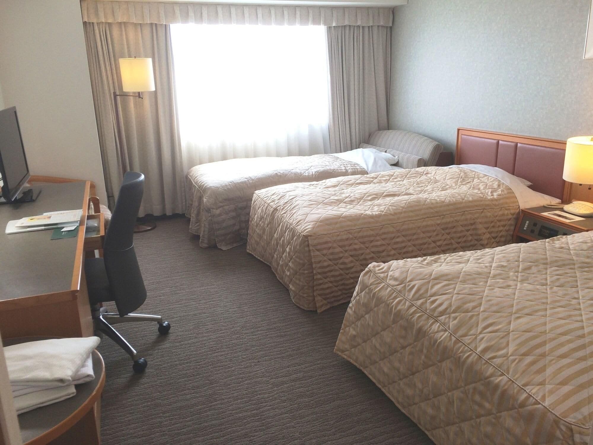 Ein Hotelzimmer mit zwei Betten, einem Schreibtisch, einem Stuhl und einem Fenster mit Vorhängen.
