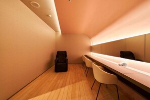 Een moderne, minimalistisch ingerichte kamer met een lang, smal bureau, twee stoelen en een zwarte tas op de vloer.