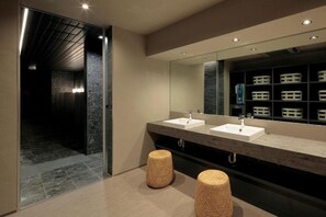 A modern bathroom with two sinks, a large mirror, and a dark hallway leading to another room.