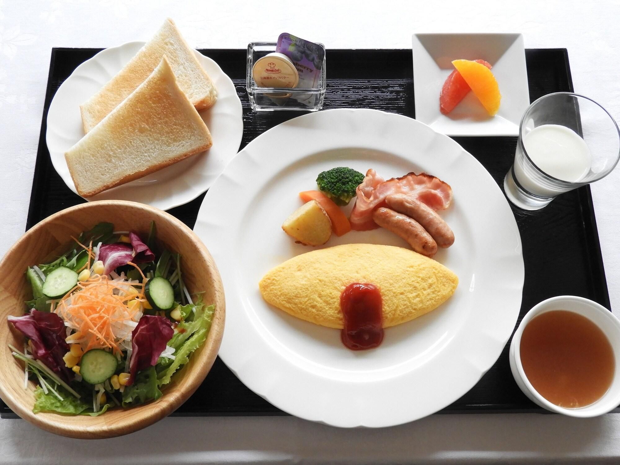 Een dienblad met geroosterde toast, een kom met salade, een omelet met ketchup, een bordje spek, een klein schaaltje bessen, een glas melk en een kop thee.