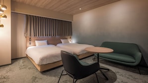Een moderne hotelkamer met twee bedden, een groene bank, een klein rond tafeltje en een zwarte stoel.