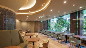 Een modern café met houten vloeren, zitplaatsen in groen en beige tinten, en een groot raam met uitzicht op groen.