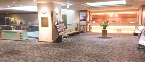 A hotel lobby with a reception desk, seating area, and a large window.